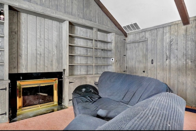 living area featuring lofted ceiling with beams, a glass covered fireplace, and wooden walls