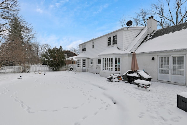 snow covered back of property with a chimney and fence