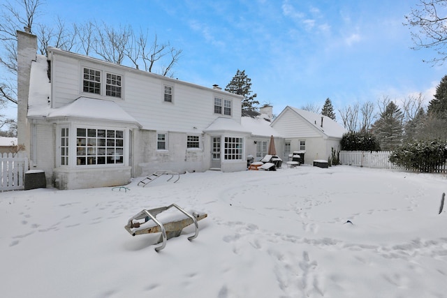 snow covered property with a garage, fence, and a chimney