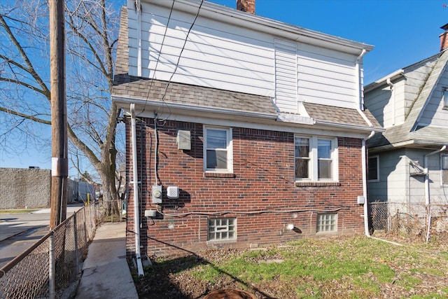 view of property exterior featuring fence private yard, a chimney, brick siding, and roof with shingles