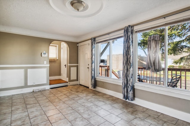 empty room with arched walkways, a textured ceiling, baseboards, and light tile patterned floors