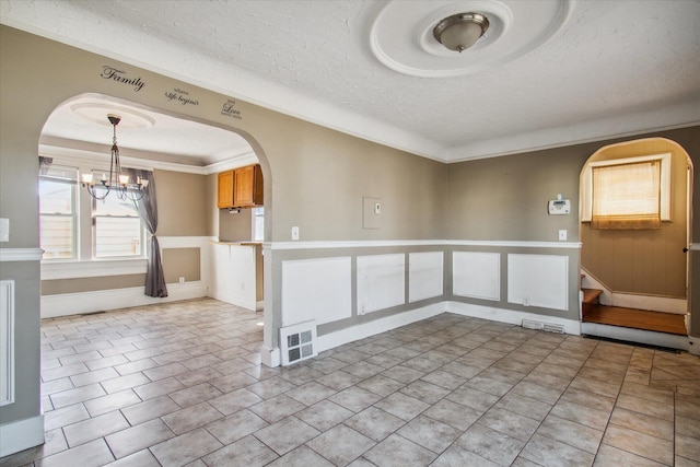 empty room with ornamental molding, arched walkways, light tile patterned flooring, and a textured ceiling