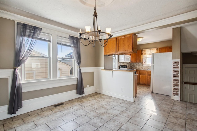 kitchen with brown cabinets, light countertops, hanging light fixtures, visible vents, and white appliances