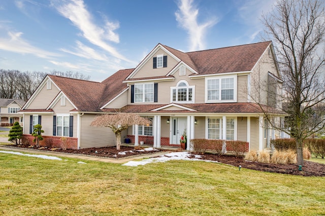 shingle-style home with brick siding, a front lawn, and roof with shingles