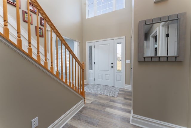 foyer entrance featuring a towering ceiling, stairs, baseboards, and wood finished floors