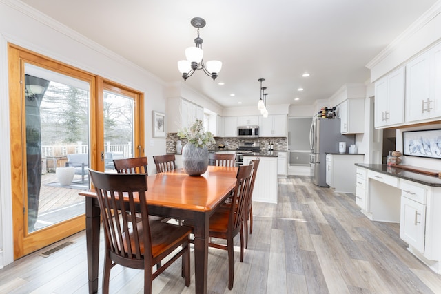 dining room featuring a chandelier, ornamental molding, light wood-type flooring, and visible vents