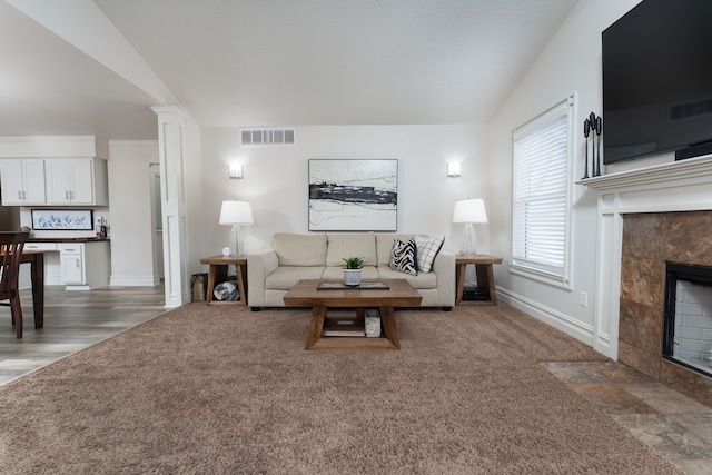 carpeted living area featuring a fireplace, ornate columns, visible vents, vaulted ceiling, and baseboards