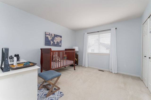 bedroom with a crib, baseboards, visible vents, light colored carpet, and a closet