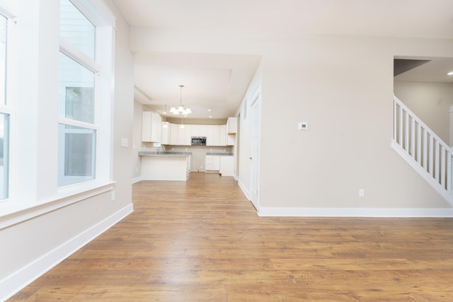 unfurnished living room featuring light wood finished floors, baseboards, stairway, a notable chandelier, and recessed lighting