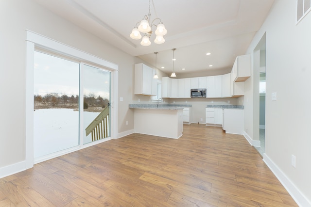 kitchen featuring visible vents, stainless steel microwave, a peninsula, light wood-style floors, and white cabinetry