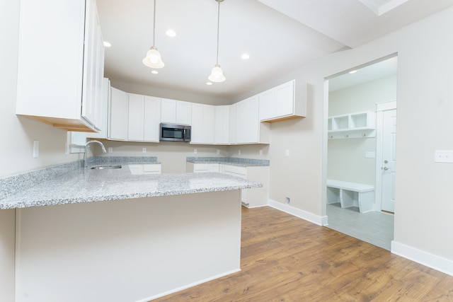 kitchen featuring white cabinets, stainless steel microwave, a peninsula, light stone countertops, and a sink