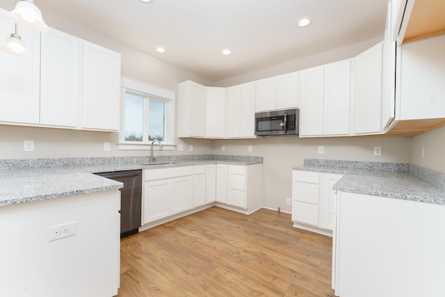 kitchen with black dishwasher, pendant lighting, stainless steel microwave, white cabinetry, and a sink