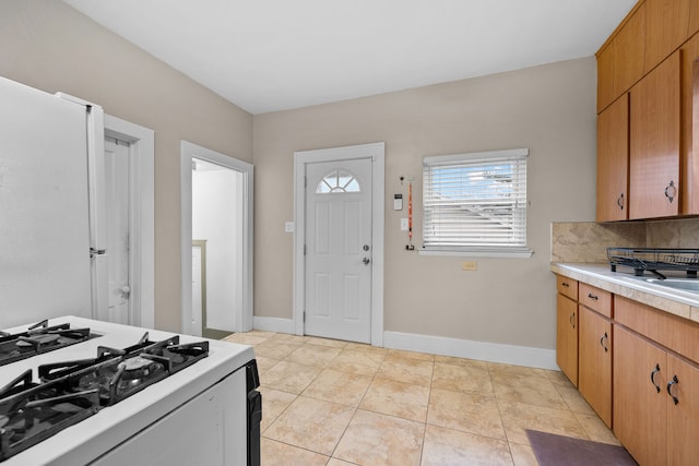 kitchen featuring gas range gas stove, light tile patterned floors, light countertops, decorative backsplash, and baseboards