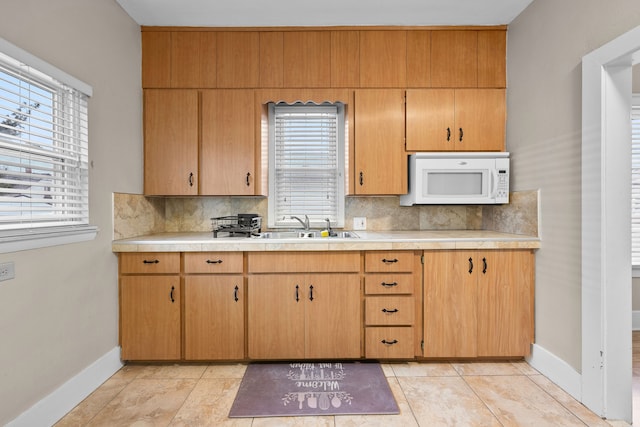 kitchen featuring light countertops, a sink, decorative backsplash, and white microwave