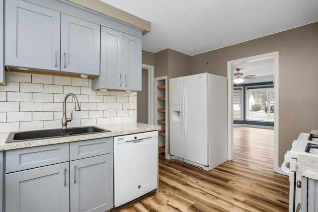 kitchen featuring gray cabinetry, light wood-style flooring, a sink, tasteful backsplash, and white appliances