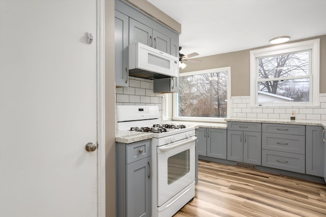 kitchen with gray cabinetry, light countertops, decorative backsplash, light wood-style flooring, and white appliances