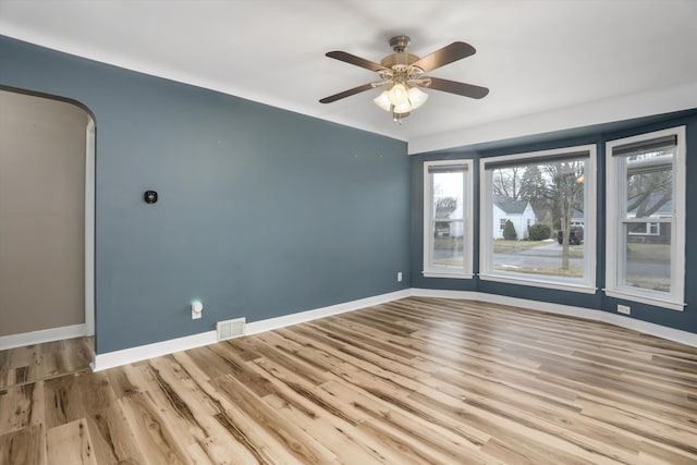 spare room featuring wood finished floors, arched walkways, visible vents, and baseboards