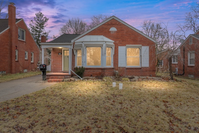 bungalow-style home with central air condition unit, brick siding, and a front lawn