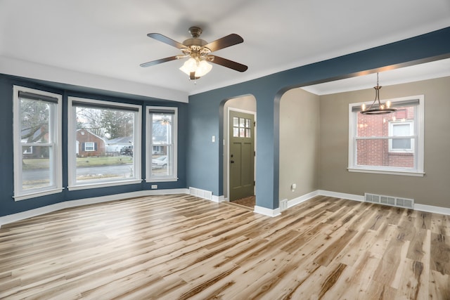 empty room featuring arched walkways, visible vents, baseboards, and wood finished floors