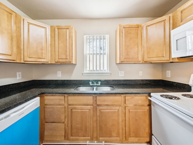 kitchen featuring light brown cabinetry, white appliances, dark stone countertops, and a sink