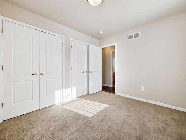 unfurnished bedroom with two closets, carpet flooring, visible vents, and baseboards