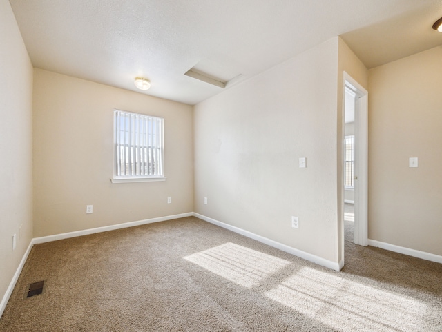 carpeted empty room featuring attic access, visible vents, and baseboards