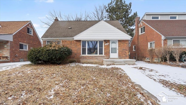 bungalow-style house with roof with shingles, a chimney, and brick siding