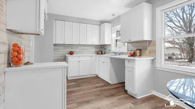 kitchen featuring decorative light fixtures, light countertops, light wood-style flooring, backsplash, and white cabinetry