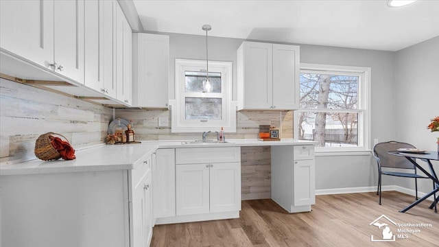 kitchen featuring tasteful backsplash, white cabinets, hanging light fixtures, and light wood-style flooring