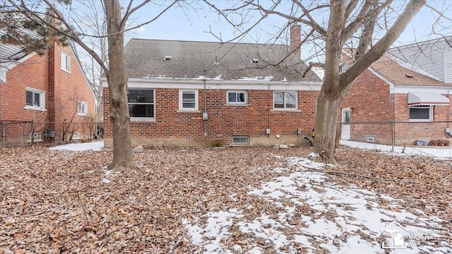 snow covered back of property with a shingled roof, brick siding, fence, and a chimney