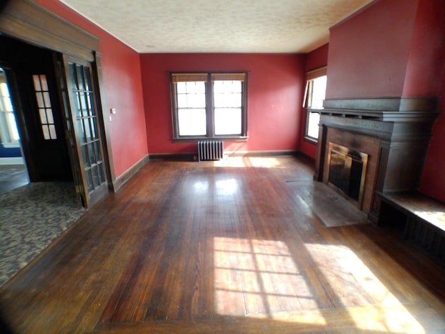 unfurnished living room featuring radiator, a fireplace with flush hearth, a textured ceiling, and wood finished floors