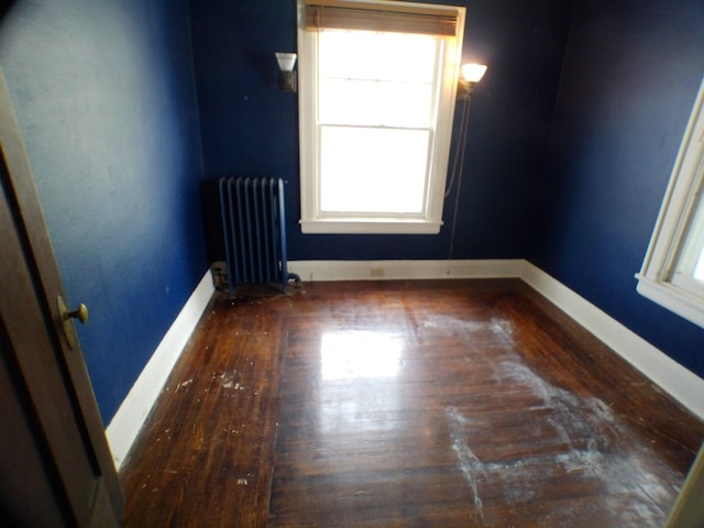 empty room featuring dark wood-type flooring, radiator heating unit, and baseboards