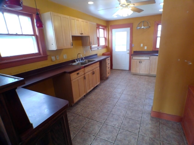 kitchen featuring light tile patterned floors, dark countertops, ceiling fan, hanging light fixtures, and a sink