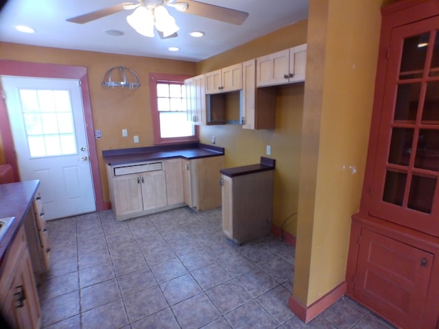 kitchen featuring light tile patterned floors, a ceiling fan, baseboards, light brown cabinetry, and dark countertops