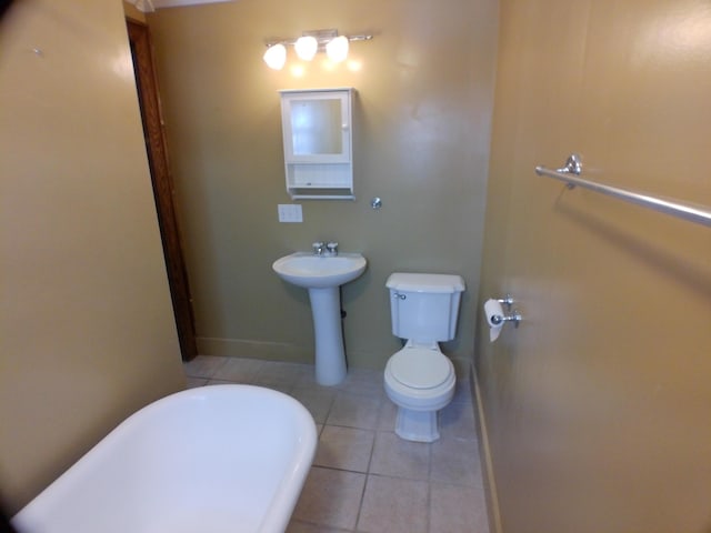 bathroom featuring tile patterned flooring, baseboards, a freestanding bath, and toilet