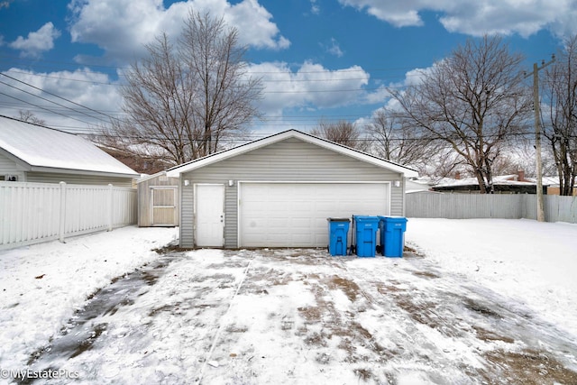 snow covered garage featuring a detached garage and fence