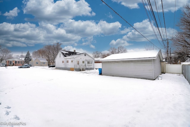 snow covered back of property with an outdoor structure and fence