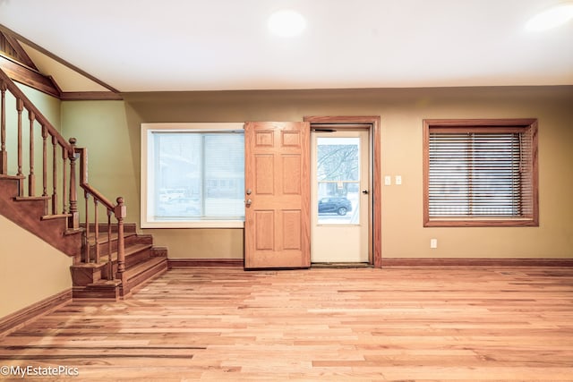 entryway featuring light wood-style floors, baseboards, stairway, and vaulted ceiling