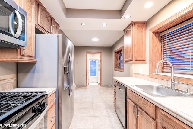 kitchen with tile countertops, stainless steel appliances, a sink, and a raised ceiling