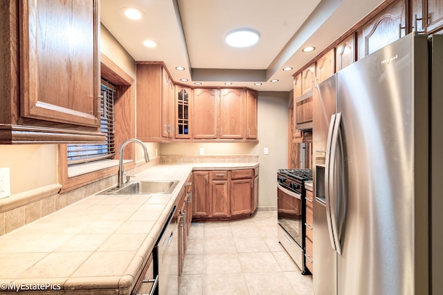 kitchen featuring range with gas stovetop, stainless steel refrigerator with ice dispenser, tile countertops, glass insert cabinets, and a sink