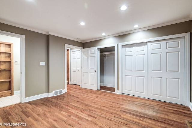 unfurnished bedroom featuring multiple closets, light wood-type flooring, visible vents, and ornamental molding