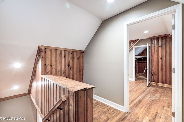 corridor featuring lofted ceiling, light wood-type flooring, and baseboards