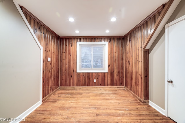 empty room with recessed lighting, baseboards, wood walls, and light wood finished floors