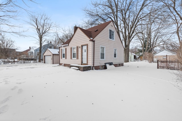 view of snowy exterior featuring a garage, a chimney, an outdoor structure, and fence