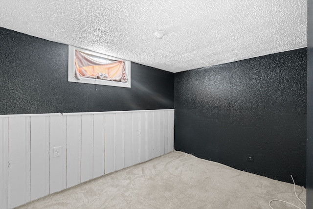 unfurnished room with light carpet, a textured ceiling, and wainscoting