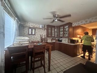 interior space with glass insert cabinets, a ceiling fan, tile patterned floors, and wallpapered walls