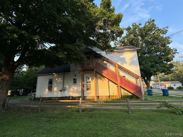 view of side of property featuring fence, stairway, and a lawn