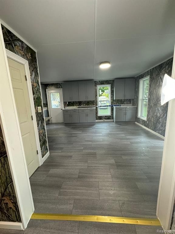 kitchen featuring wallpapered walls, baseboards, dark wood-style floors, and gray cabinetry