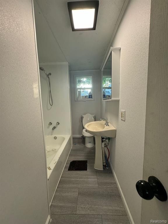 bathroom featuring toilet, baseboards, tub / shower combination, and a sink