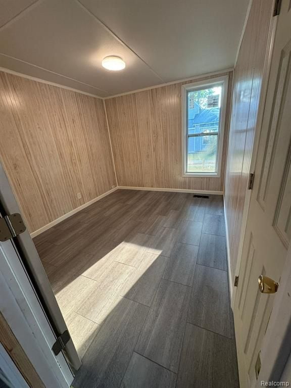 spare room featuring dark wood-type flooring, visible vents, wooden walls, and baseboards